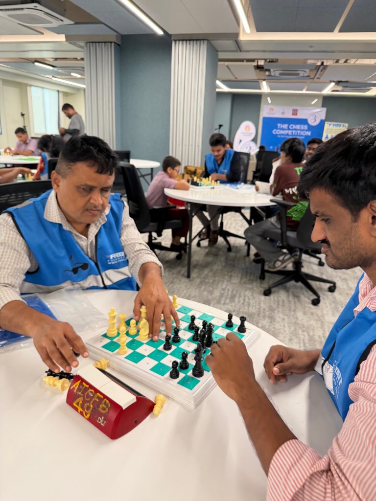 Two participants in reflective jackets play chess at a tournament table.
