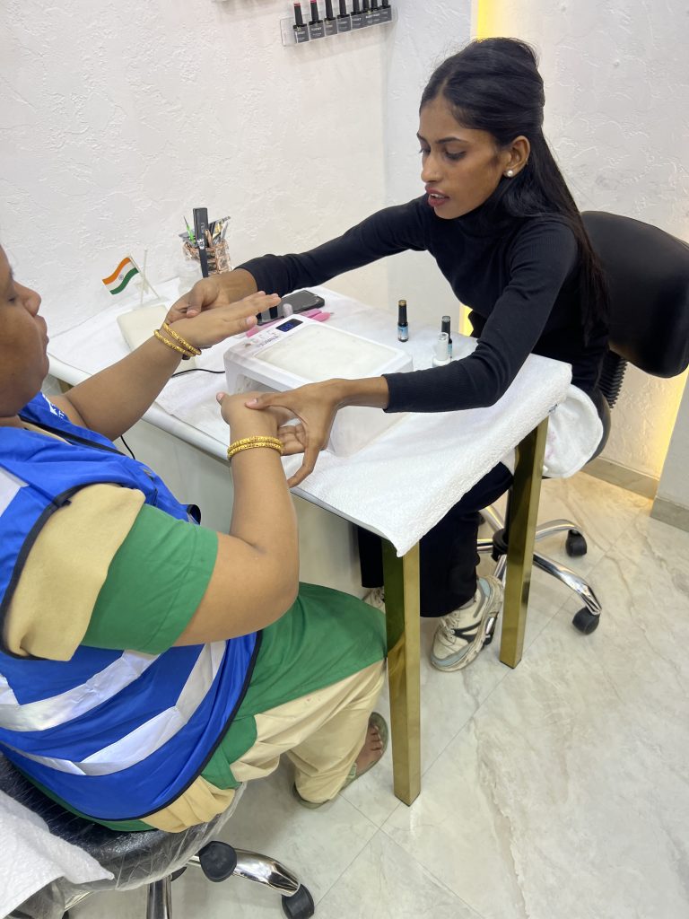 A participant in a blue reflective jacket has her nails tended to during a salon visit.